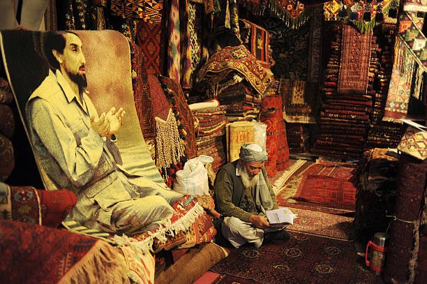KABUL, AFGHANISTAN - OCTOBER 17: An Afghan shopowner surrounded by carpets and rugs seen sits behind a rug imprinted with image of assasinated Afghan Mujahedin commander Ahmad Shah Massoud in his shop in Chicken Street on October 17, 2011 in Kabul, Afghanistan. Chicken Street has been a focus for Afghanistan tourists since the days of the Hippy Trail. All kinds of handicrafts are available here, from jewellery to carpets,  antique muskets to poached furs. (Photo by Kaveh Kazemi/Getty Images)