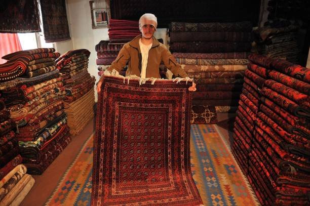 TO GO WITH STORY 'Afghanistan-Iran-economy-carpets' by Mushtaq Mojaddidi

In this photograph taken on March 3, 2012 an Afghan shopkeeper displays a carpet to customers in his shop on Chicken Street in Kabul.   For decades Ismail Temorzada's handmade Afghan carpets decorated people's homes around the world, but export problems and competition from Iran's machine-made products have left his business threadbare. "My carpet sales are down, no one is buying hand-made carpets anymore," says Temorzada,45, who has run a shop for more than 20 years in Kabul's once crowded and colorful Chicken Street bazaar. "Iranian machine made carpets are imported to Afghanistan at a cheaper price," he told AFP, dismissing them as lacking originality, durability and charm. But they are cheap and people buy them, and his sales have dropped by 70 percent over the past year, he says. Carpets are Afghanistan's best known export, woven mostly by women in the north of the country.   Displaying his best carpets, from Andkhoy in northern Faryab province, Temorzada said they cost 60,000 Afghanis -- about 1,300 US dollars -- but nobody is buying them now.   AFP PHOTO/ MASSOUD Hossaini (Photo by MASSOUD HOSSAINI / AFP) (Photo by MASSOUD HOSSAINI/AFP via Getty Images)