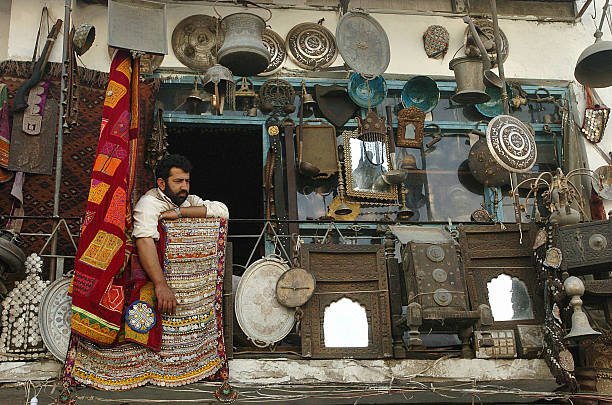 Kabul, AFGHANISTAN: An Afghan shopkeeper sits amongst antiques and curios displayed outside his shop on the famous Chicken Street in Kabul, 23 June 2007. Chicken Street has for decades been popular with foreigners attracted by the carpets and antiques sold there.     AFP PHOTO/SHAH Marai (Photo credit should read SHAH MARAI/AFP via Getty Images)